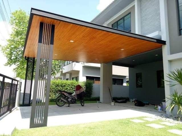 Mái che khoảng sân trước biệt thự với trần tông gỗ và cụm thanh đứng ở góc mái; bên dưới có khu vực để xe máy.