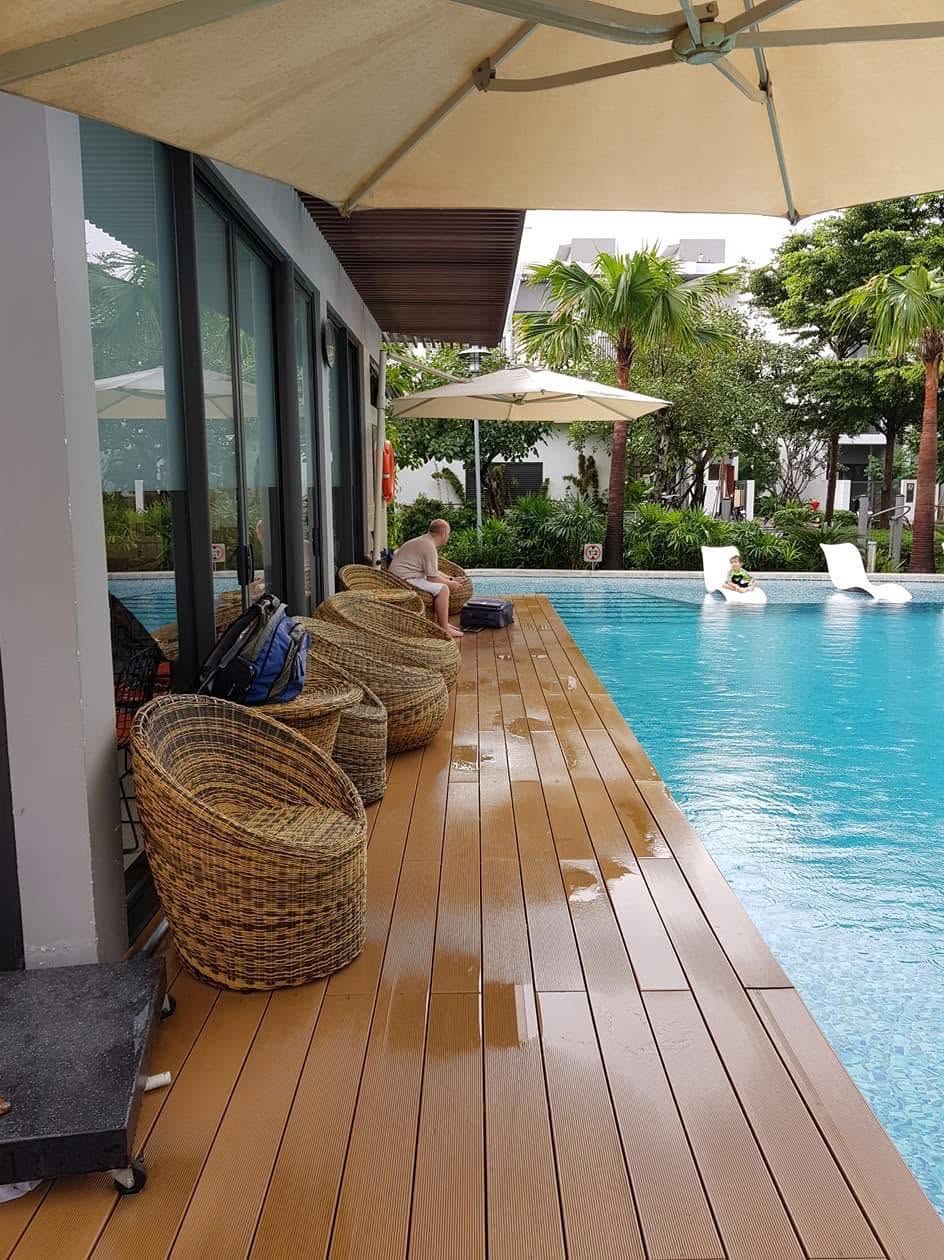 Lối sàn gỗ chạy dọc hồ bơi, cạnh khu ghế ngồi và tán che; gợi ý cách dành một dải nghỉ bên mép nước.