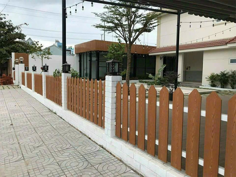 Hàng rào thanh đứng màu gỗ xen trụ xây màu trắng, tạo ranh giới mở ở sân trước
